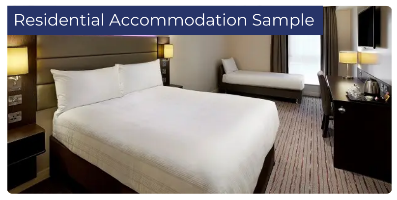 Sample residential accommodation room featuring a double bed, desk with chair, flat-screen TV, lamps, and an additional single bed, designed for student comfort.