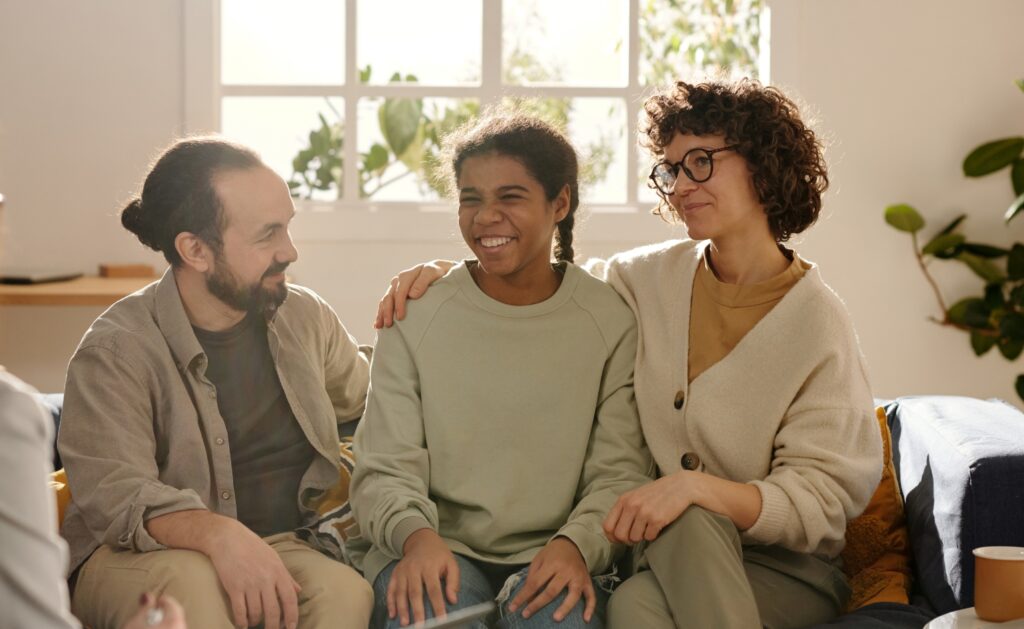 A friendly host family sitting together with a smiling student in a warm, welcoming home environment. Become a Host – caring and supportive at UK Guardians.